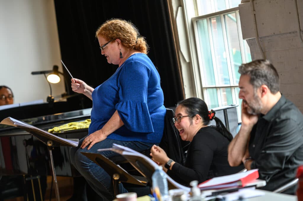 Conductor Rosemary Thomson holding a conductors baton rehearsing the opera Shawnadithit