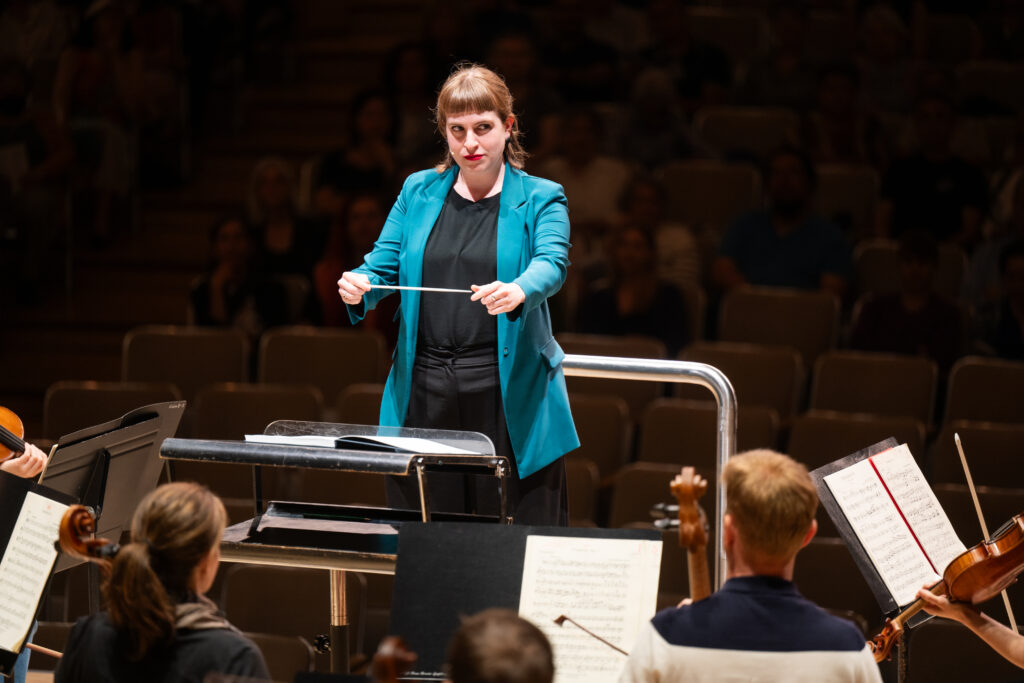Conducting Fellow Juliane Gallant stands on the conducting podium, holding the baton between her two hands.