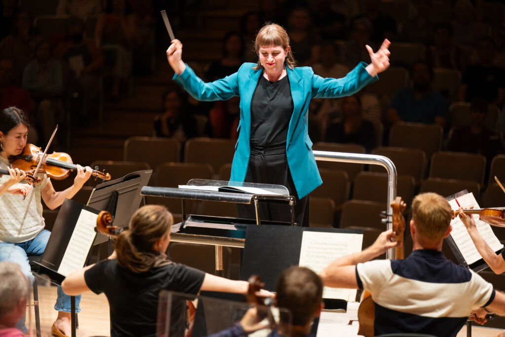 Conducting Fellow Juliane Gallant stands on the conducting podium, holding the baton in her right hand.