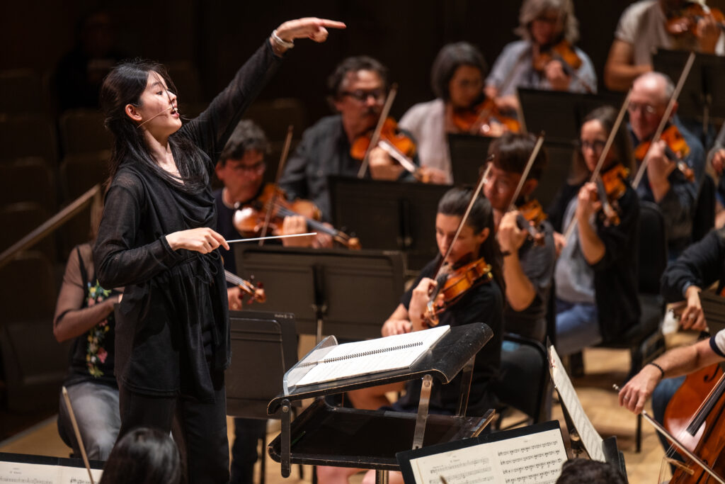 Conducting Fellow Monica Chen stands on the conducting podium.