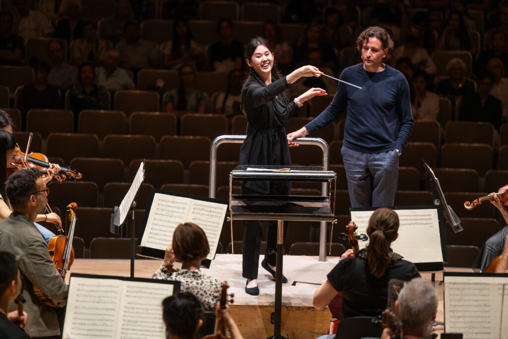 Conducting Fellow Monica Chen stands on the conducting podium.