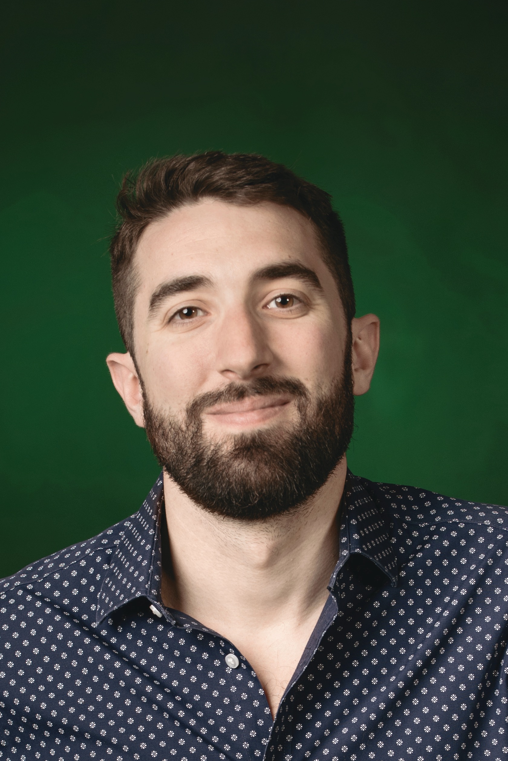Smiling face of Pierre-André Doucet short brown hair and beard, wearing grey collared shirt.
